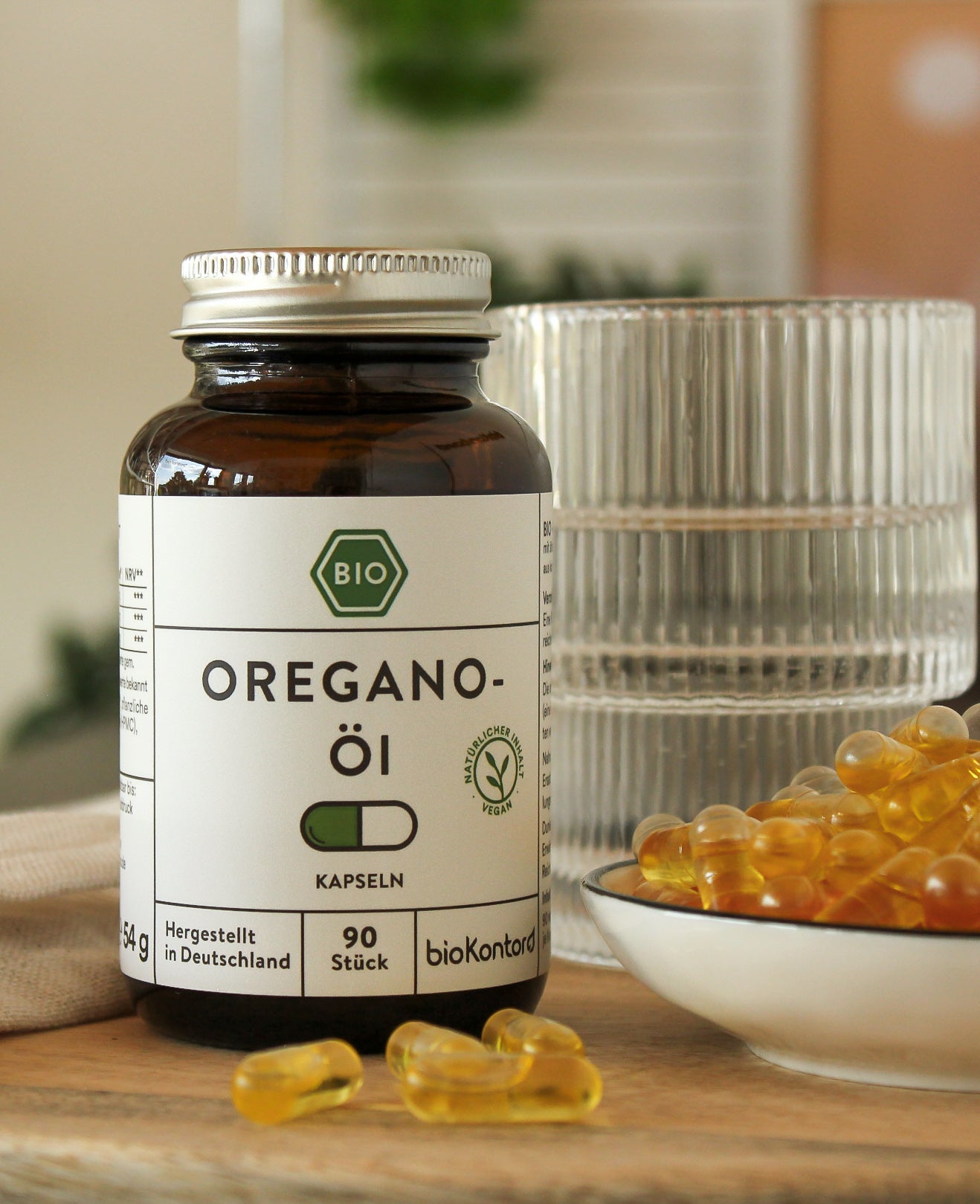 Oreganoöl Kapseln  in Glasdose mit einem Glas Wasser und veganen Kapseln in der Küche